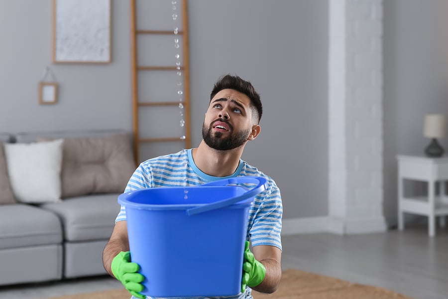 Young Man Collecting Leaking Water From Ceiling At Home, Space F Get Your Leak Repaired