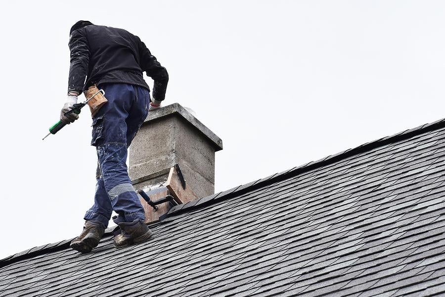 Roofer Construction Worker Repairing Chimney On Grey Slate Shingles Roof Of Domestic House, Sky Back Jack C. Wilson Roofing Co.