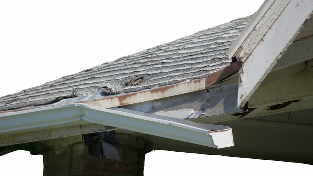 Damaged roof shingles and a detached white gutter on a coastal home, highlighting professional salt air roof damage repair in Jacksonville.